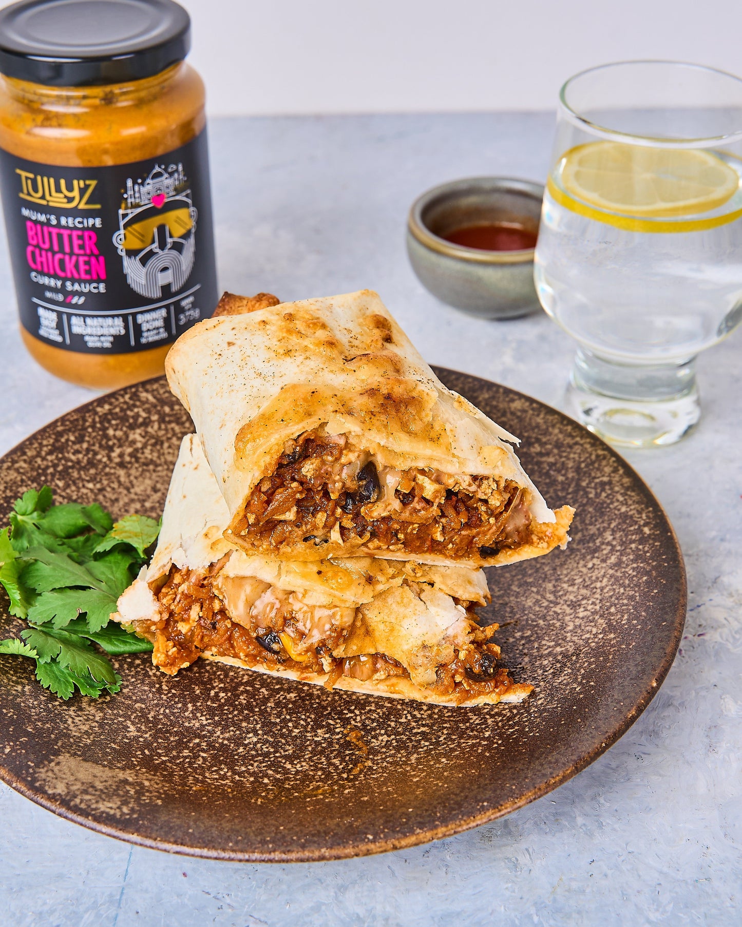 A close-up of a Butter Chicken Tofu Burrito wrapped in a tortilla, garnished with fresh coriander.