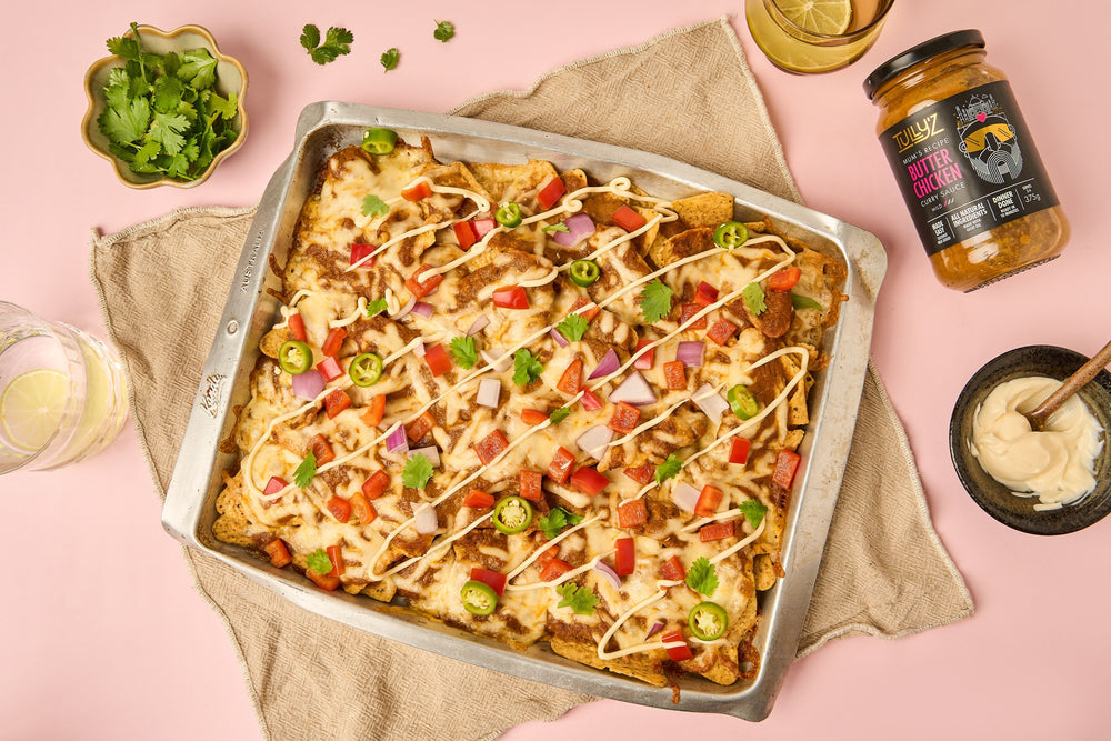 A plate of Butter Chicken Nachos topped with melted cheese, diced tomatoes, onion, and green peppers.